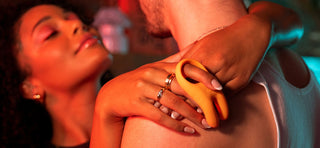 Woman wrapping her arms around man's neck and holding his shoulders, holding an orange cock ring in her fingers