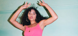 Woman in pink singlet with pouted lips and hands in the air against light blue wall