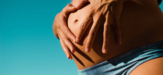 Close up of pregnant belly with hands in heart shape around belly button