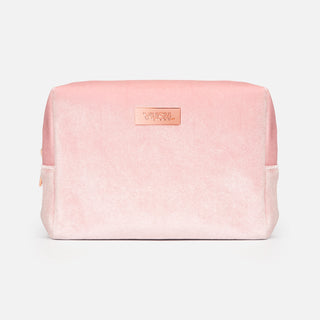 Pink soft cosmetics bag made of fuzzy velvet-like material with rose gold plaque that reads "VUSH" against light grey background