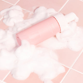 150ml pink bottle with white pump lid and white text that reads "VUSH IT'S ALL GOOD INTIMATE WASH" placed against pink tiles with white foam surrounding bottle