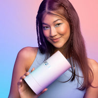 Young woman with long dark hair smiling and wearing a baby blue tank top while holding blue/purple/pink gradient cylinder packaging that reads 